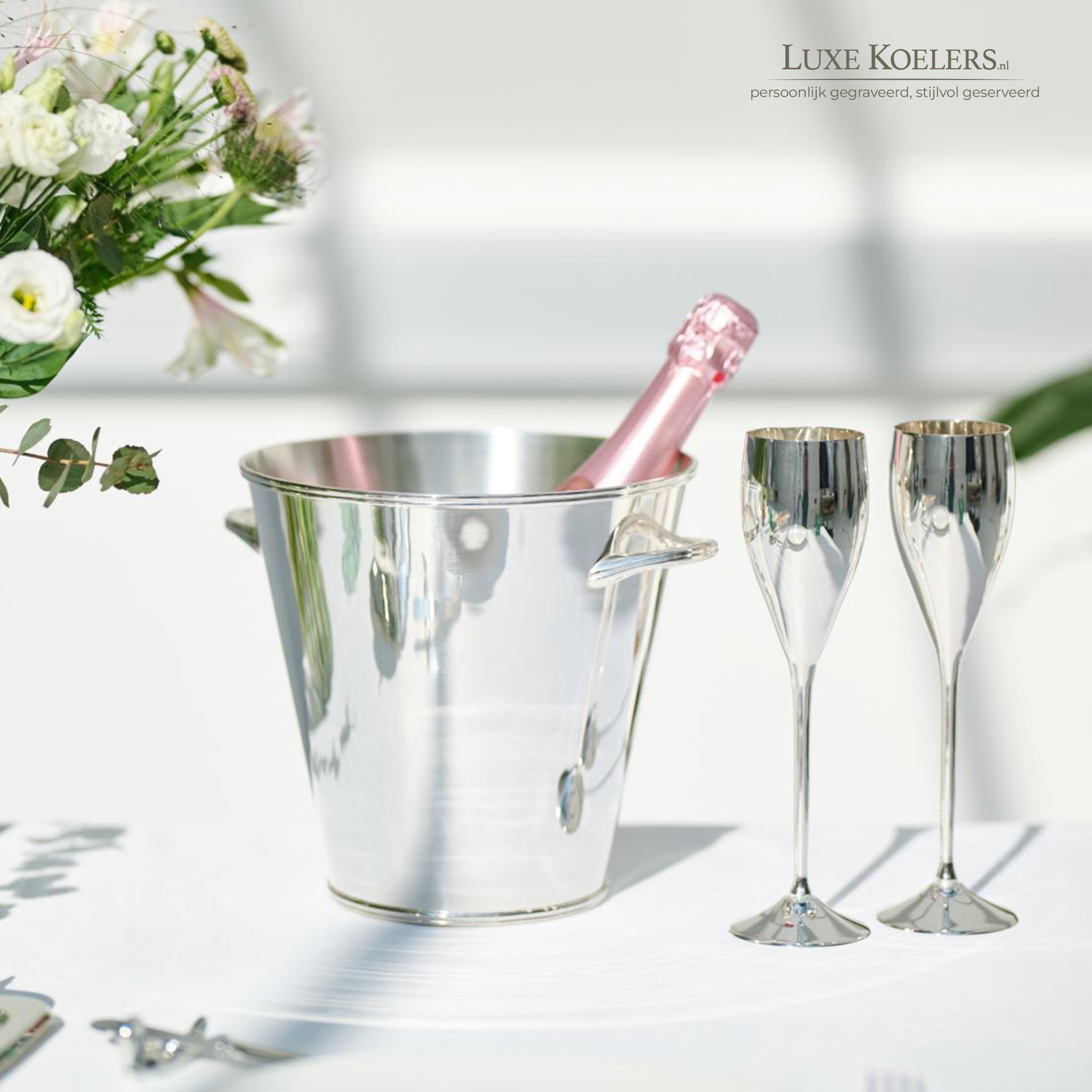 verzilverde koeler en 2 verzilverde flutes voor champagne op witte tafel